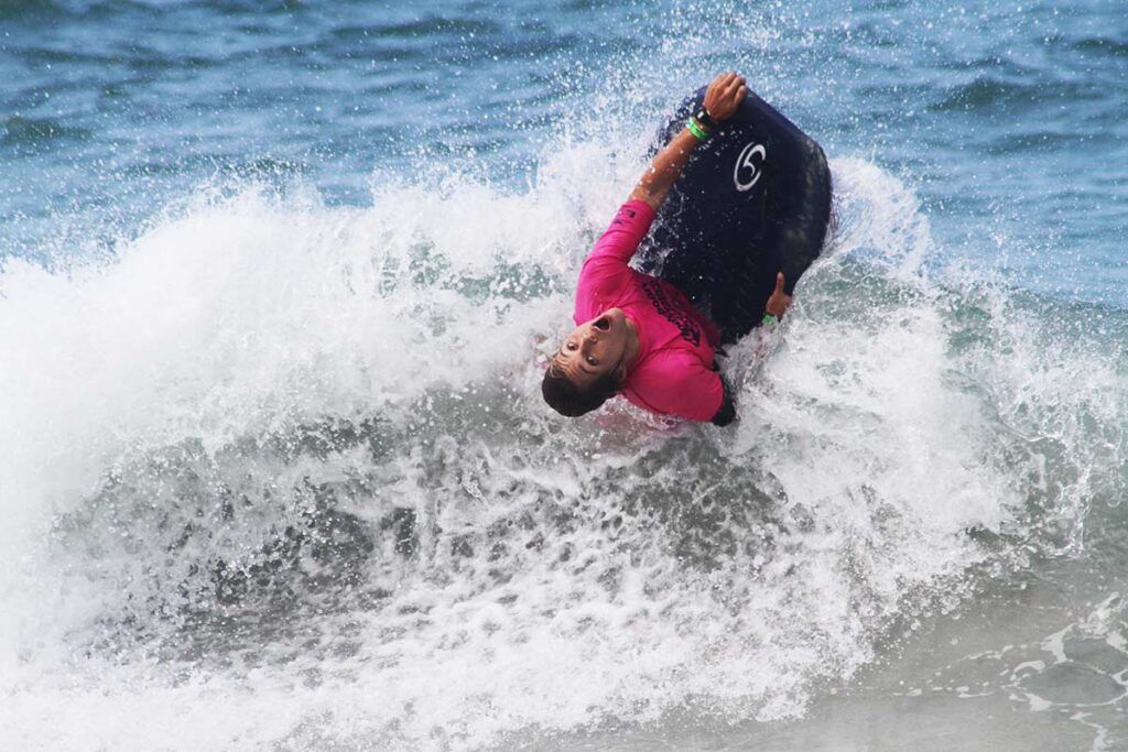 Man doing a bodyboarding trick in a pink rashguard.